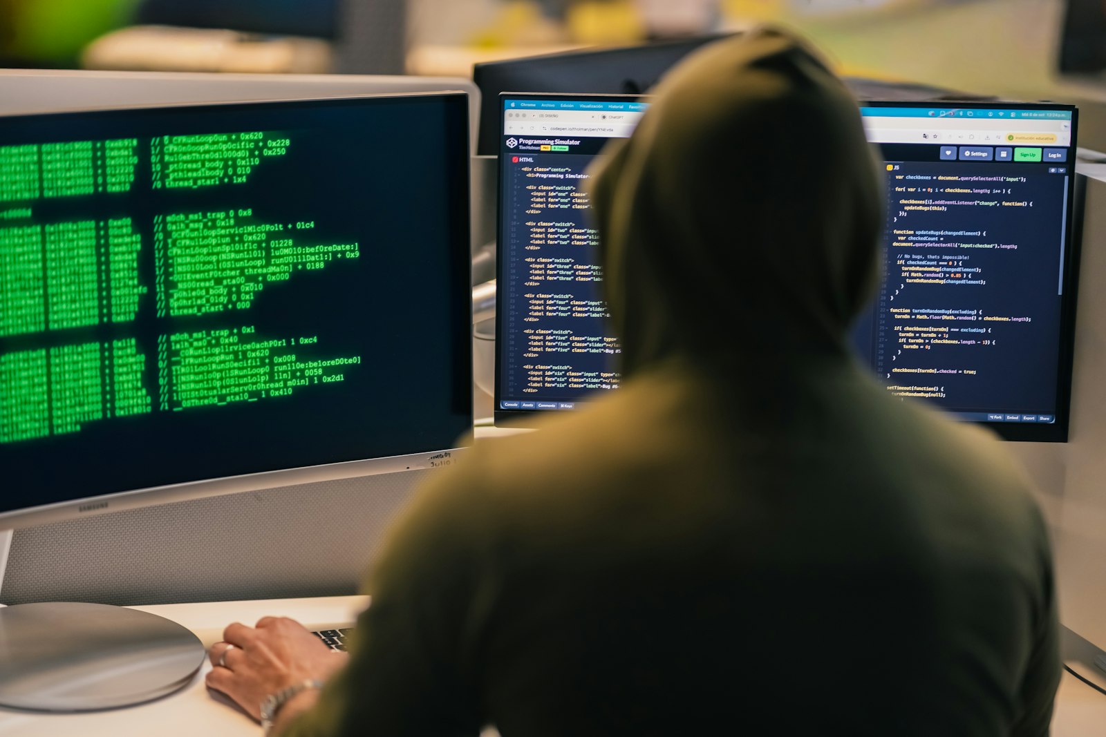 Person in a hoodie working at several computer screens