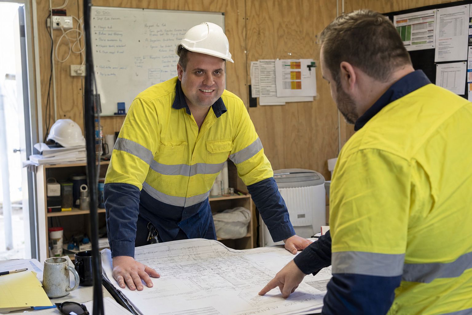 Brandon from Defy IT in hi-vis going over drawings with a site supervisor in a construction site office